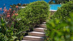 Escadaria de pedra que leva a uma piscina com vista para o mar e colinas.