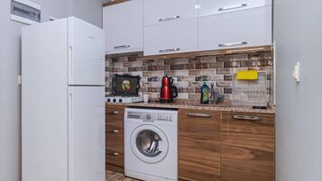 Una cucina compatta con un frigorifero bianco, una lavatrice, mobili in legno e un rivestimento a piastrelle.