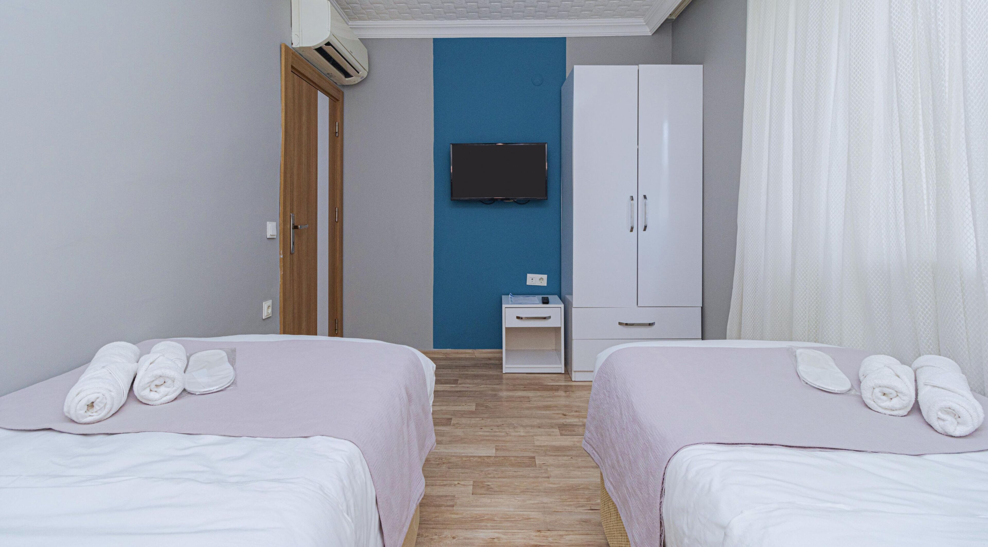 Ein Hotelzimmer mit zwei Betten, einem an der Wand montierten Fernseher, einem Kleiderschrank und einem kleinen Nachttisch.