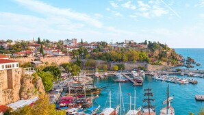 Une ville côtière dotée d’un fort historique, d’un port de plaisance où sont amarrés différents types de bateaux, et d’immeubles résidentiels situés sur une colline.