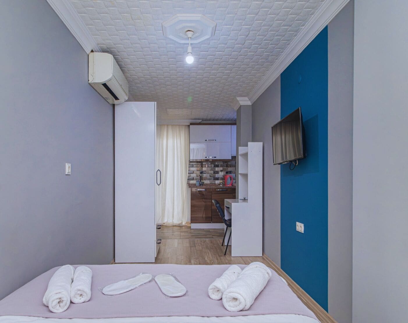 A hotel room with a bed, a TV, and a kitchenette in the background.