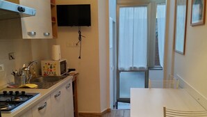 Une cuisine compacte équipée d’une cuisinière à gaz, d’un évier et d’un téléviseur à écran plat fixé au-dessus de l’évier. On y trouve également un coin repas avec une table et des chaises, ainsi qu’une fenêtre qui laisse entrer la lumière naturelle.