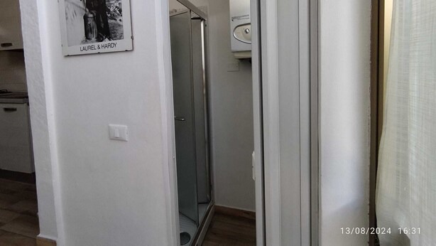 Un couloir étroit avec une porte vitrée donnant sur une salle de bain. Une photographie en noir et blanc de Laurel et Hardy est accrochée au mur.