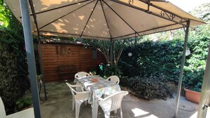 Une terrasse extérieure avec une table et des chaises sous une pergola, entourée de verdure.