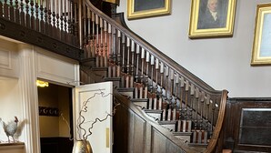 A grand staircase with ornate railings, a round wooden table with a brass vase, and a checkered floor pattern. - A former hotel set deep in the Dorset countryside in a small village (Chettle)