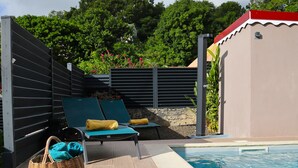 A poolside area with two lounge chairs, a wicker basket, and a small building with a red roof. - Charming vacation home (Sainte-Anne)