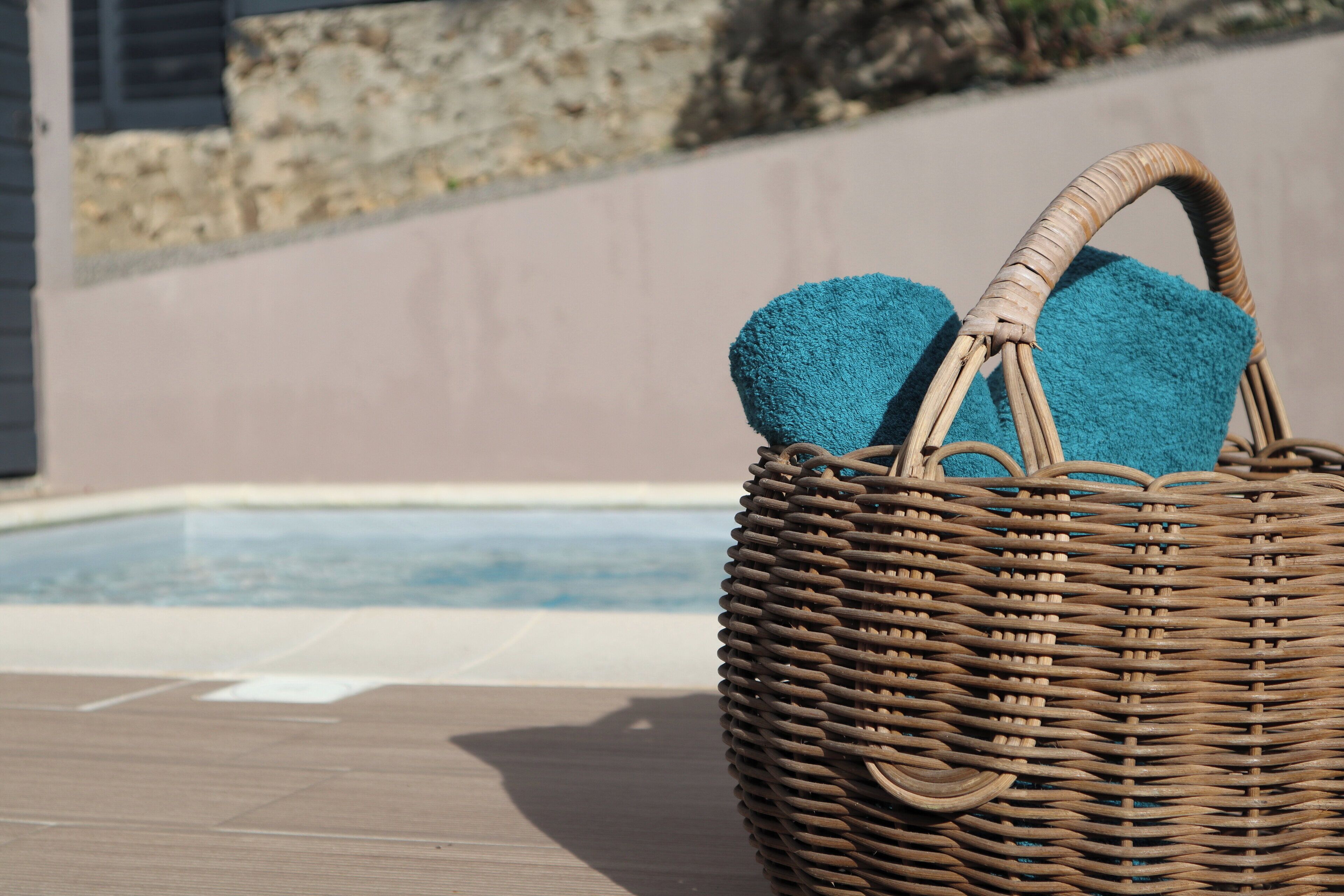 A wicker basket with towels on a wooden deck near a pool.