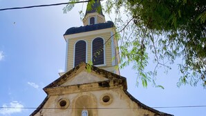 A church with a bell tower, a blue door, and statues on the facade. - Charming vacation home (Sainte-Anne)