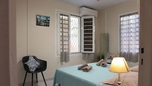 A bedroom with a bed, a chair, a lamp, and a painting on the wall. - Charming vacation home (Sainte-Anne)