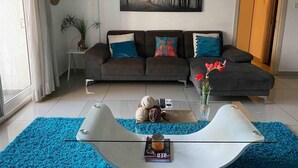 A modern living room with a sectional sofa, a coffee table, and a painting of a forest. - Immaculate 1-bed Apartment in the Heart of Accra (Accra)