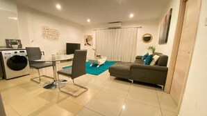 A modern living room with a dining area, a sofa, a TV, and a washing machine. - Immaculate 1-bed Apartment in the Heart of Accra (Accra)