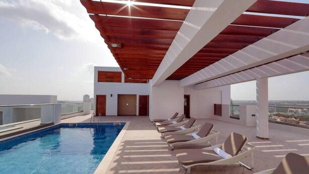 A rooftop pool area with a clear view of the city skyline, modern architecture, and a series of sun loungers. - Immaculate 1-bed Apartment in the Heart of Accra (Accra)
