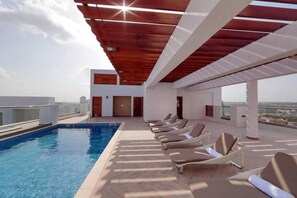 A rooftop pool area with a clear view of the city skyline, modern architecture, and a series of sun loungers. - Immaculate 1-bed Apartment in the Heart of Accra (Accra)