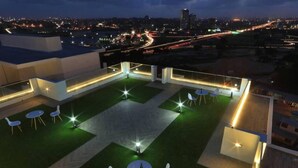 A rooftop terrace with a central lawn area, surrounded by seating arrangements and illuminated by ambient lighting. - Immaculate 1-bed Apartment in the Heart of Accra (Accra)