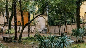 An outdoor garden area with various plants and trees, a stone bench, and a wall with a circular opening. - Casa Ambrosini - Atena Apt by Wonderful Italy (Bologna)