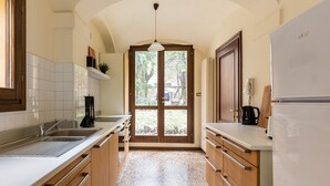A kitchen with white countertops, wooden cabinets, a built-in oven, and a large window with a view of the outdoors. - Casa Ambrosini - Atena Apt by Wonderful Italy (Bologna)