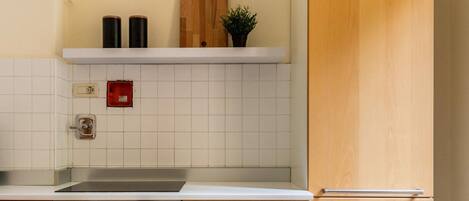 A kitchen with white tiled walls, a wooden cabinet, a built-in oven, and a hanging light fixture.