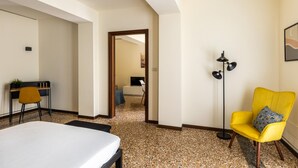 A hotel room with a bed, a desk, a yellow armchair, a floor lamp, and a painting on the wall. - Casa Ambrosini - Atena Apt by Wonderful Italy (Bologna)