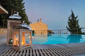 A swimming pool with a wooden deck, a small building with a chimney, and a lit lantern. - Paxoi Serene Oasis - Mylos  Mediterranean Charm (Arvanitakeika)