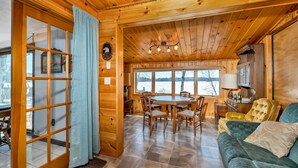 L’intérieur d’un chalet en bois comprend un coin repas, un canapé et de grandes fenêtres donnant sur un paysage enneigé.