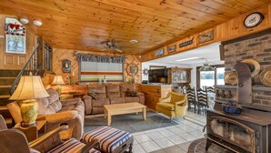 L’intérieur chaleureux d’un chalet avec un plafond en bois, une cheminée, un coin repas et un salon comprenant un canapé et des fauteuils.