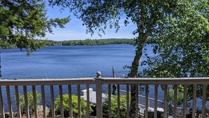 Une terrasse en bois avec une rambarde donnant sur un lac, entourée d’arbres et bordée par une rive éloignée.