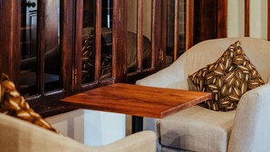 A room with a wooden cabinet, a beige armchair, a patterned pillow, and a red carpet with a floral design. - Yushili Hotel & Restaurant (Kampala)