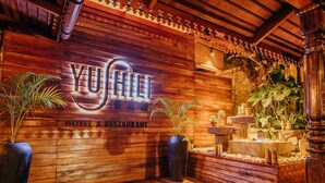 A wooden wall with the sign "YU SHILI HOTEL & RESTAURANT" and a small indoor garden with plants and a water feature. - Yushili Hotel & Restaurant (Kampala)