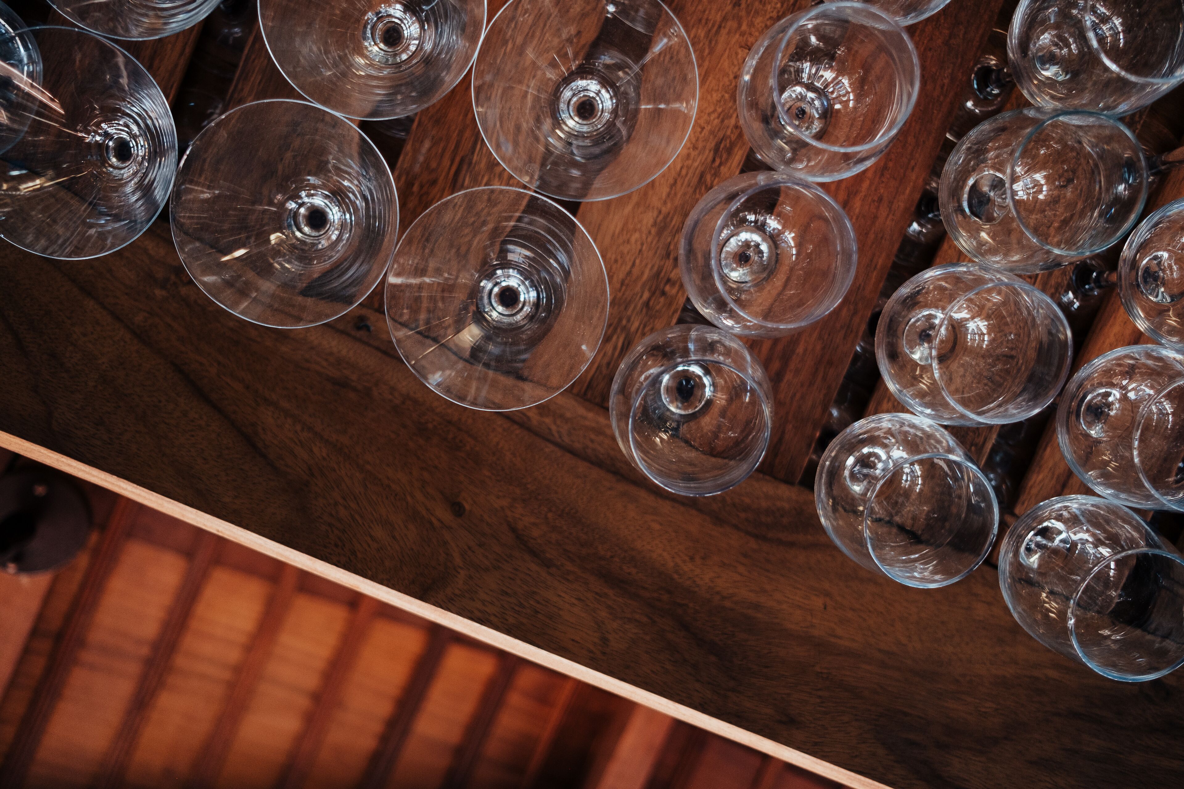 A wooden table with multiple clear wine glasses arranged on it.