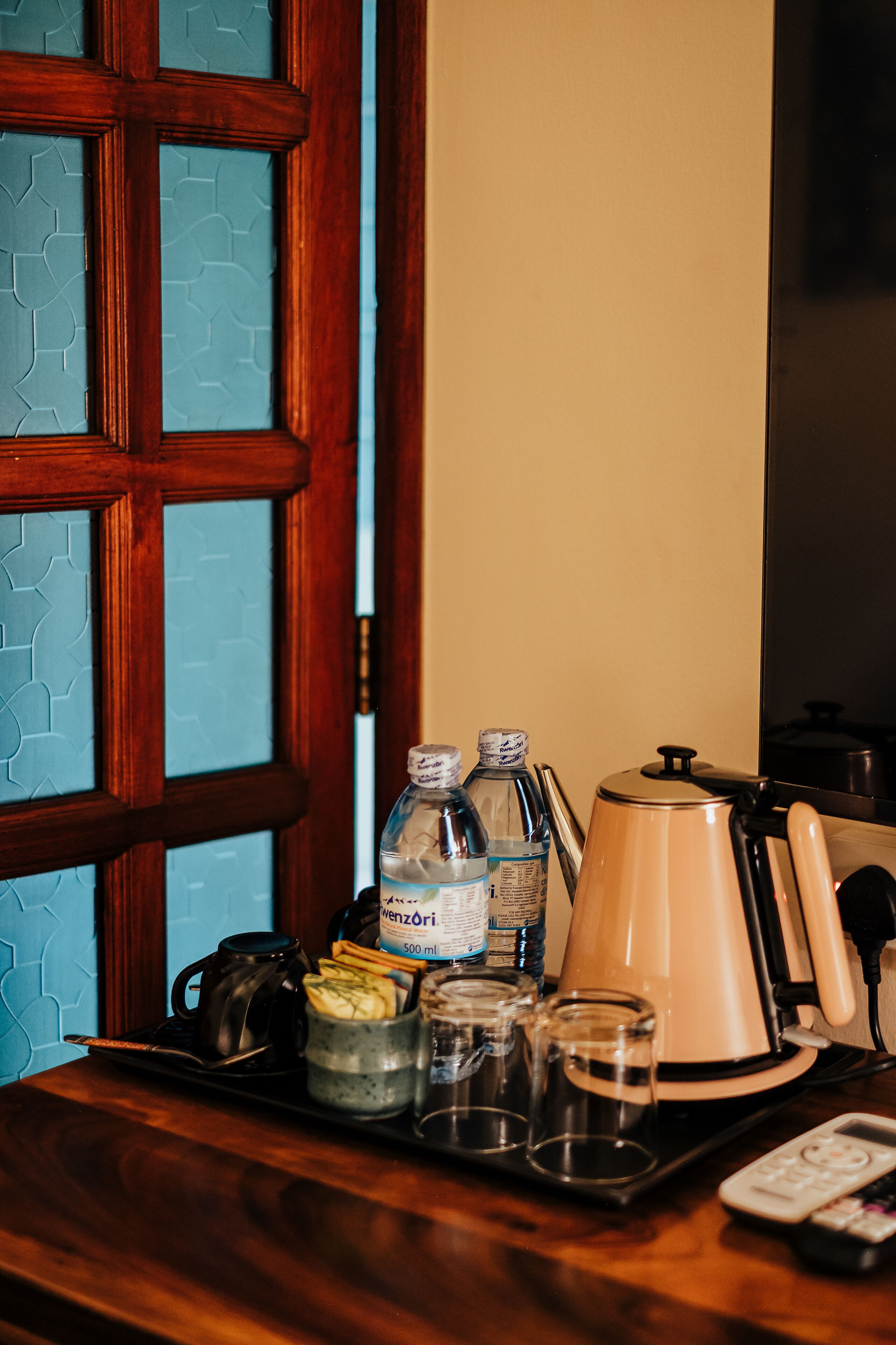 A kitchen counter with a coffee maker, water bottles, a kettle, and a remote control.