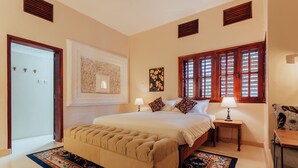 A bedroom with a large bed, two bedside tables with lamps, a decorative rug, and a window with shutters. - Yushili Hotel & Restaurant (Kampala)