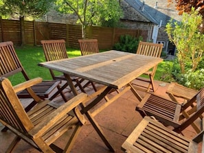 Une table de patio en bois, accompagnée de quatre chaises, entourée d’un sol en briques et d’une clôture en bois.
