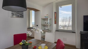 Een eethoek met een houten tafel, rode stoelen, een zwarte lamp en een raam met uitzicht op de lucht en bomen.