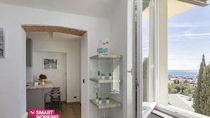 Een modern appartement met een keukenhoekje, een glazen schap en uitzicht op de stad door een groot raam.