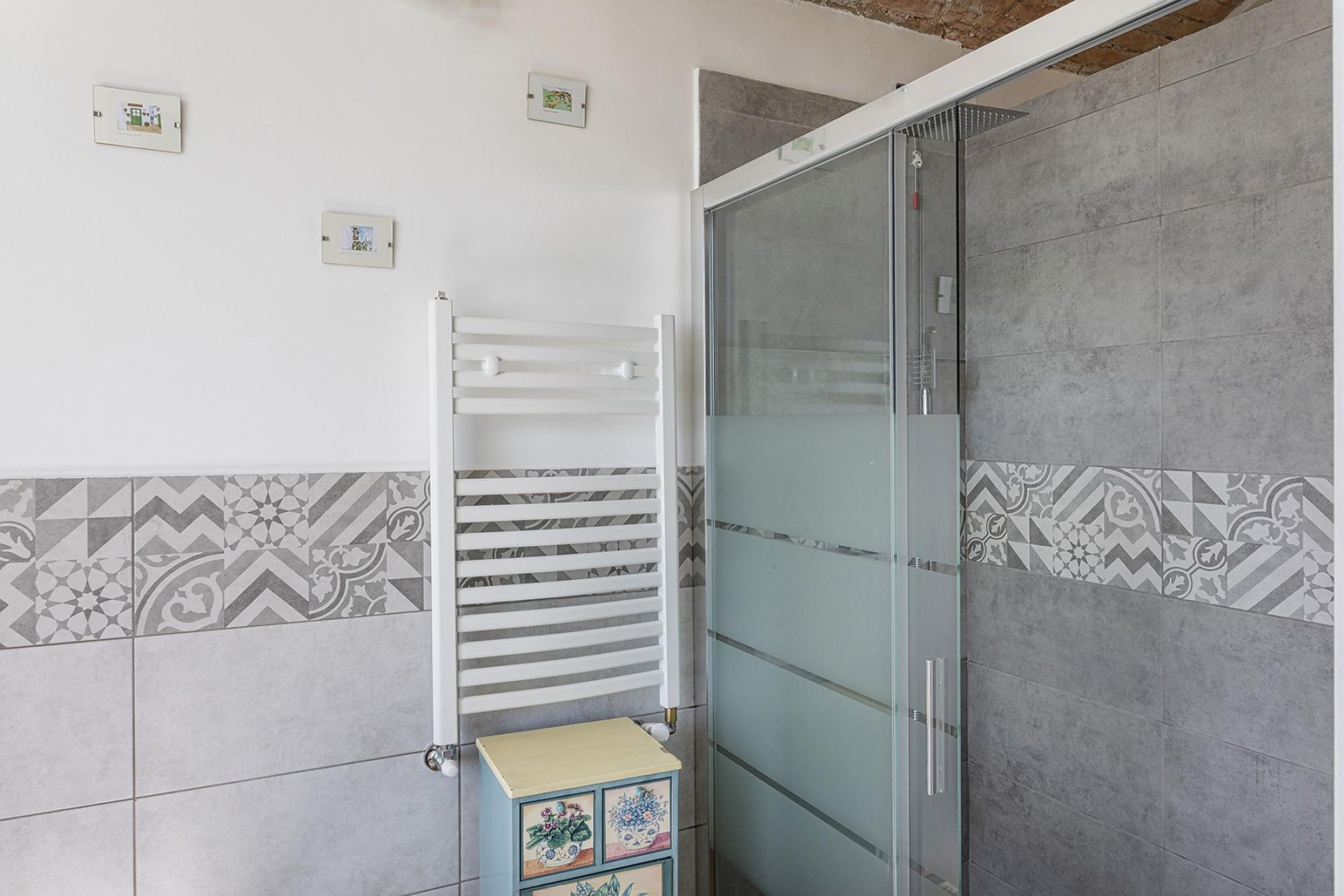 A bathroom with a glass shower enclosure, a white towel rack, and a small decorative cabinet.
