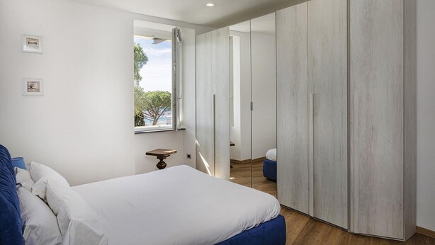 Een slaapkamer met een bed, een kledingkast, een raam en een klein tafeltje.