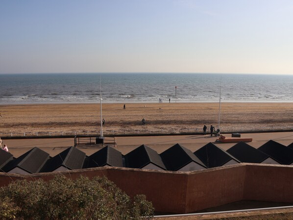 Une vue sur la côte, avec une plage, une promenade bordée d’édifices à l’architecture moderne et un ciel dégagé.