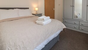 A neatly made bed with a folded white towel, a bedside lamp, and a grey wardrobe with a mirror. - Flat 8 (Bridlington)