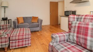 A living room with a grey sofa, plaid armchairs, and a wooden floor. - Flat 8 (Bridlington)