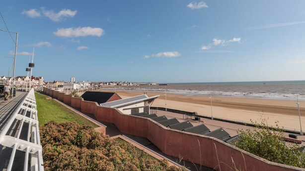A coastal promenade with a beach, steps leading down to the shore, and a row of buildings in the background. - Flat 8 (Bridlington)