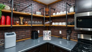 A kitchen with brick walls, shelves with kitchenware, a coffee maker, and a microwave. - Take a trip to the Industrial Age in this centrally-located townhome. (Springdale)