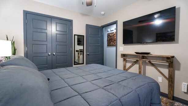A bedroom with a large bed, a TV mounted on the wall, and a wooden bench. - Take a trip to the Industrial Age in this centrally-located townhome. (Springdale)