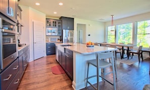 A modern kitchen with a central island, wooden flooring, and a dining area with a table and chairs.