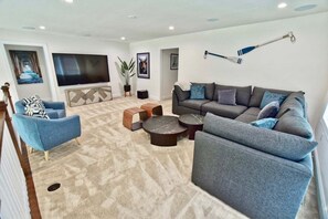 A modern living room with a grey sofa, blue armchair, and a flat-screen TV mounted on the wall.