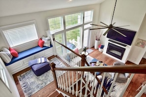 A staircase leading to a balcony with a view of a lawn, a fireplace, and a ceiling fan.