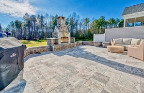 A patio with stone flooring, a stone fireplace, wicker furniture, and a covered grill.