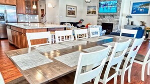 Una cocina amplia con una isla central, un comedor con una mesa larga y sillas, y una sala de estar con chimenea.
