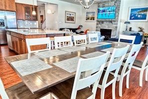 Una cocina amplia con una isla central, un comedor con una mesa larga y sillas, y una sala de estar con chimenea.
