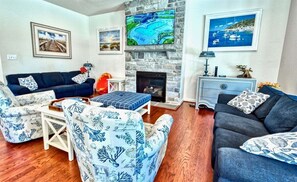 A living room with a stone fireplace, a sofa, a coffee table, and a TV mounted on the wall.