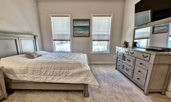 Une chambre à coucher avec un lit, une commode et deux fenêtres équipées de stores.